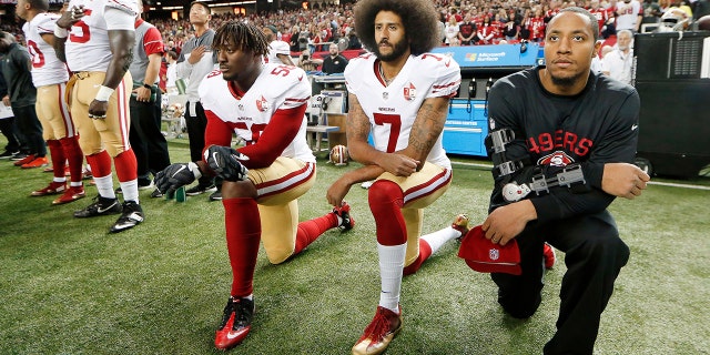 El mariscal de campo de los 49ers, Colin Kaepernick (centro), se arrodilla durante un partido de la NFL para protestar contra la brutalidad policial.