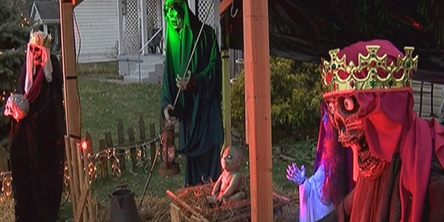 The nativity scene features life-size figures and a zombie baby Jesus, with pale skin and pure white eyes. At night, the figures are illuminated by red and green lights.