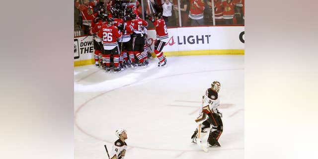 Anaheim Ducks goalie Frederik Andersen (31) and teammate Cam Fowler (4) skate off the ice as the Chicago Blackhawks celebrate their 5-4 win during the second overtime in Game 4 of the Western Conference finals of the NHL hockey Stanley Cup playoffs, Saturday, May 23, 2015, in Chicago. (AP Photo/Charles Rex Arbogast)
