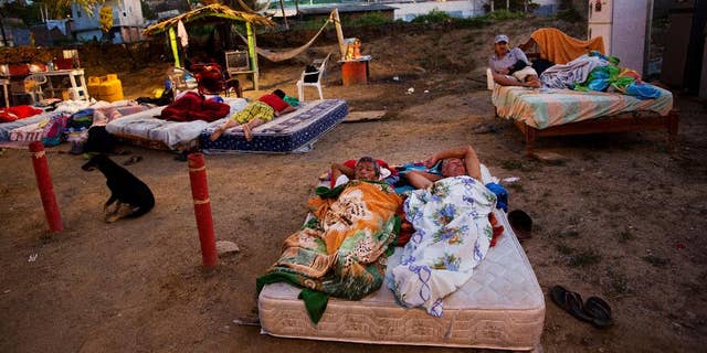 In this Wednesday, April 20, 2016 photo, neighbors Carlos Bardales, left, and Cesar Filay, share a mattress as they sleep outside their collapsed homes damaged by a 7.8-magnitude earthquake, in Manta, Ecuador. Hundreds of aftershocks have rattled the country since last Saturday night's quake and Ecuadoreans are still sleeping outside and struggling to find food and water. (AP Photo/Rodrigo Abd)