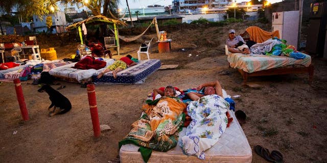 In this Wednesday, April 20, 2016 photo, neighbors Carlos Bardales, left, and Cesar Filay, share a mattress as they sleep outside their collapsed homes damaged by a 7.8-magnitude earthquake, in Manta, Ecuador. Hundreds of aftershocks have rattled the country since last Saturday night's quake and Ecuadoreans are still sleeping outside and struggling to find food and water. (AP Photo/Rodrigo Abd)