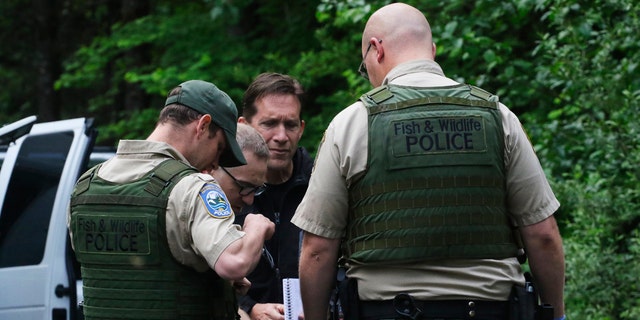 Washington State Fish and Wildlife Police confer with an individual from the King County Medical Examiner's and a King County Sheriff's deputy on a remote gravel road above Snoqualmie, WA., following a fatal cougar attack. Saturday May 19, 2018.