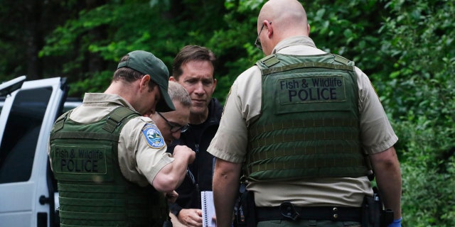 Washington State Fish and Wildlife Police confer with an individual from the King County Medical Examiner's and a King County Sheriff's deputy on a remote gravel road above Snoqualmie, WA., following a fatal cougar attack. Saturday May 19, 2018.