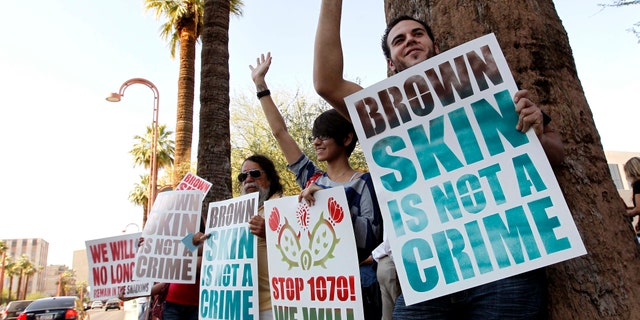 Laurent Taillefer, right, and Andrea Begay, second from right, both of Phoenix, wave at cars as they honk their horns driving by as the two join immigration rights protesters as they gather after the United States Supreme Court decision regarding Arizona's controversial immigration law, SB1070, at the local U.S. Immigration and Customs Enforcement offices Monday, June 25, 2012, in Phoenix. The Supreme Court struck down key provisions of Arizonaâs crackdown on immigrants Monday but said a much-debated portion on checking suspectsâ status could go forward. (AP Photo/Ross D. Franklin)