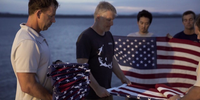 Eric Terrill, co-founder of Project Recover and an oceanographer from Scripps Institution of Oceanography at the University of California San Diego, holds a stack of American flags commemorating the 11 crew members loss when “Heaven Can Wait” crashed. The Project Recover team conducts a commemorative flag folding ceremony at the location of each crash site they discover. (Project Recover)