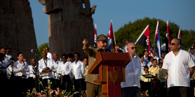 Cuba's President Raul Castro speaks at a podium as Vice President Jose Ramon Machado, second from right, stands by during celebrations marking Revolution Day in Guantanamo, Cuba, Thursday, July 26, 2012. Cuba marks the 59th anniversary of the July 26, 1953 rebel attack led by Fidel and Raul Castro on the Moncada military barracks. The attack is considered the beginning of the revolution that culminated with dictator Fulgencio Batista's ouster. (AP Photo/Ramon Espinosa)
