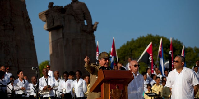 Cuba's President Raul Castro speaks at a podium as Vice President Jose Ramon Machado, second from right, stands by during celebrations marking Revolution Day in Guantanamo, Cuba, Thursday, July 26, 2012. Cuba marks the 59th anniversary of the July 26, 1953 rebel attack led by Fidel and Raul Castro on the Moncada military barracks. The attack is considered the beginning of the revolution that culminated with dictator Fulgencio Batista's ouster. (AP Photo/Ramon Espinosa)