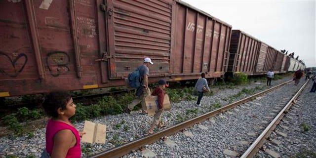 In this July 12, 2014, photo, migrants walk along the rail tracks after getting off a train during their journey toward the U.S.-Mexico border in Ixtepec, Mexico. The surge in unaccompanied minors and women with children migrating from Central America has put new attention on decades-old smuggling organizations.  (AP Photo/Eduardo Verdugo)