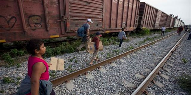 In this July 12, 2014, photo, migrants walk along the rail tracks after getting off a train during their journey toward the U.S.-Mexico border in Ixtepec, Mexico. The surge in unaccompanied minors and women with children migrating from Central America has put new attention on decades-old smuggling organizations. (AP Photo/Eduardo Verdugo)