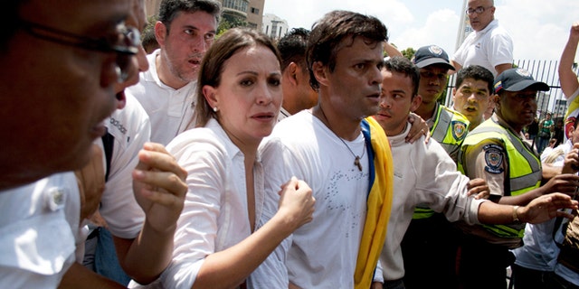 Venezuelan congresswoman Maria Corina Machado, left, and opposition leader Leopoldo Lopez, center, are surrounded by anti-government demonstrators before Lopez surrenders to national guards, in Caracas, Venezuela, Tuesday, Feb 18, 2014. Lopez re-emerged from days of hiding to address an anti-government demonstration and then surrendered to authorities Tuesday in a move that he said will open the world's eyes to the increasingly authoritarian bent of Venezuela's socialist government.(AP Photo/Juan Manuel Hernandez)
