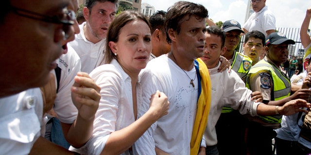 Venezuelan congresswoman Maria Corina Machado, left, and opposition leader Leopoldo Lopez, center, are surrounded by anti-government demonstrators before Lopez surrenders to national guards, in Caracas, Venezuela, Tuesday, Feb 18, 2014. Lopez re-emerged from days of hiding to address an anti-government demonstration and then surrendered to authorities Tuesday in a move that he said will open the world's eyes to the increasingly authoritarian bent of Venezuela's socialist government.(AP Photo/Juan Manuel Hernandez)