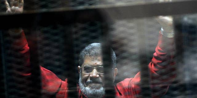 FILE - In this June 21, 2015 file photo, former Egyptian President Mohammed Morsi, wearing a red jumpsuit that designates he has been sentenced to death, raises his hands inside a defendants cage in a makeshift courtroom at the national police academy, in an eastern suburb of Cairo, Egypt. An Egyptian court struck down on Tuesday, Nov. 22, 2016 a life sentence and ordered the retrial of ousted Islamist President Mohammed Morsi on charges of conspiring with foreign militant groups, including the Palestinian Hamas. The decision comes nearly 17 months after the initial sentence against Morsi, who hails from the now-banned Muslim Brotherhood. Along with Morsi's life sentence, those of 16 others, including the group's spiritual leader Mohammed Badei, were thrown out. (AP Photo/Ahmed Omar, File)