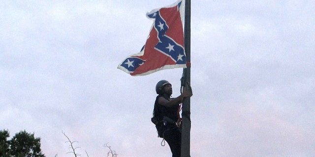 Bree Newsome of Charlotte, N.C., climbs a flagpole to remove the Confederate battle flag at a Confederate monument in front of the Statehouse in Columbia, S.C., on Saturday, June, 27, 2015. She was taken into custody when she came down. The flag was raised again by capitol workers about 45 minutes later. (AP Photo/Bruce Smith)