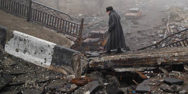 An elderly woman walks across a destroyed bridge, fallen onto the road towards the airport, the scene of heavy fighting in Donetsk, Ukraine, Sunday, March 1, 2015. The recent pullback of some weapons from the line separating government and rebel forces in Ukraine seems to have boosted the prospects for peace, although both sides are warning of their readiness to resume fighting if necessary. (AP Photo/Vadim Ghirda)