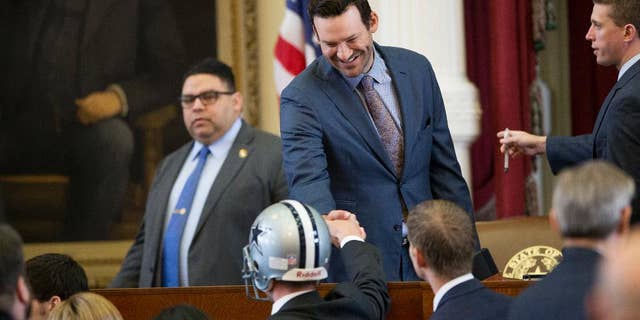 State Rep. Jeff Leach, R-Plano, wearing a football helmet, shakes hands with former Dallas Cowboys quarterback Tony Romo, who was honored in the House Chamber at the Capitol in Austin, Texas, on Wednesday May 3, 2017. (Jay Janner/Austin American-Statesman via AP)