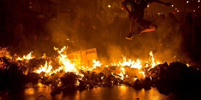 AP10ThingsToSee - A demonstrator jumps over a burning barricade at the Cinelandia Square during a march in support of teachers on strike in Rio de Janeiro on Monday, Oct. 7, 2013. Teachers have been on strike demanding better pay for nearly two months. (AP Photo/Felipe Dana, File)