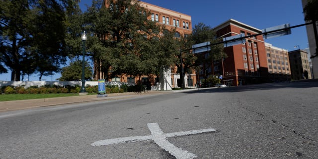FILE- In this Nov. 12, 2013 file photo, an X marks the spot on Elm Street where the first bullet hit President John F. Kennedy on Nov. 22, 1963 near the former Texas School Book Depository, now known as the Sixth Floor Museum, background, on Dealey Plaza in Dallas. The Xs on the street are gone. The disappearance of the marks come as the city on Friday is set to mark the 50th anniversary of the assassination of John F. Kennedy with a solemn ceremony in Dealey Plaza. (AP Photo/LM Otero, File)