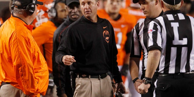 FILE - Oklahoma State head coach Mike Gundy, center, talks with defensive coordinator Bill Young, left, and officials, right, during the fourth quarter of an NCAA college football game against Texas Tech in Stillwater, Okla., in this Nov. 17, 2012 file photo. Defensive coordinator Bill Young _ a coaching veteran of 45 years _ has said he doesn't know how much longer he plans to coach, although he talked Thursday Dec. 20, 2012 about recruiting and next season as if he will be back.(AP Photo/Sue Ogrocki, File)