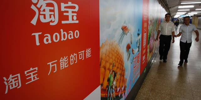 FILE - In this Sept. 18, 2014 file photo, people walk past an advertising billboard showing the mobile app of Alibaba’s Taobao consumer-to-consumer site at a subway station in Beijing. Alibaba Group Holding Ltd. reports quarterly financial results before the market opens on Wednesday, Aug. 12, 2015. (AP Photo/Vincent Thian, File)