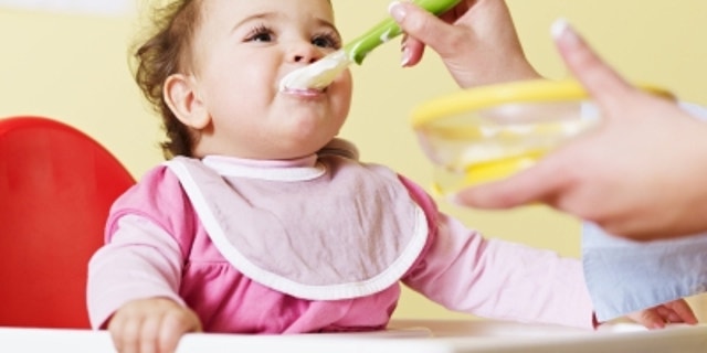 mom giving homogenized food to her daughter on high chair. Horizontal shape
