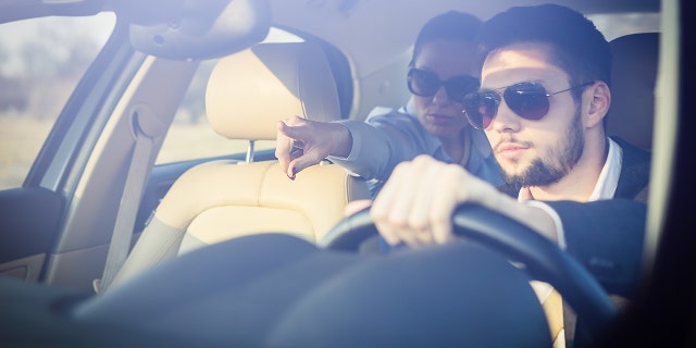 Business woman showing direction to chauffeur from the back of a car