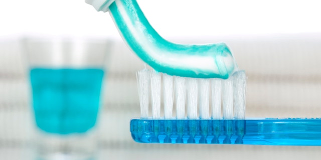 A blue toothbrush with toothpaste. Mouthwash and towels on the background