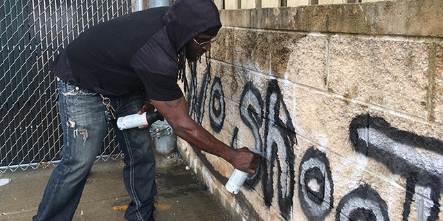 In this Wednesday, Aug. 2, 2017, photo Tyree Colion spray paints the words "No Shoot Zone" on a brick wall behind a convenience store, in a spot near where a 13-year-old girl was fatally shot in Baltimore County, Md. County police later arrested Colion for what they say was destruction of property, although he claimed he was given permission to paint the wall by a store clerk. (AP Photo/Juliet Linderman)
