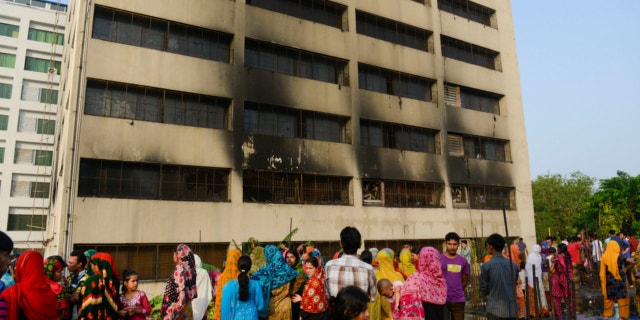 May 9, 2013: Workers stand outside an 11-story building that houses the Tung Hai Sweater Ltd. factory and apartments after a fire in Dhaka, Bangladesh.