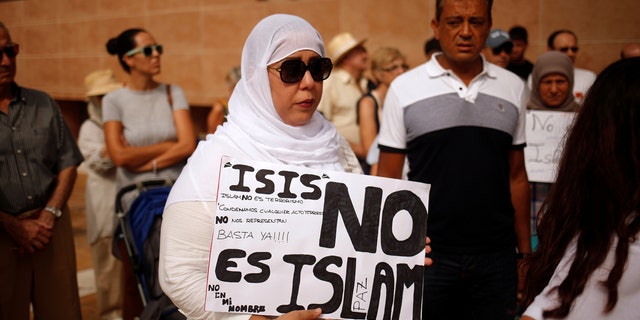 A Muslim woman holds a sign that reads "ISIS is not Islam" as she takes part in a gathering of different religious groups in rejection of the attack in Barcelona.