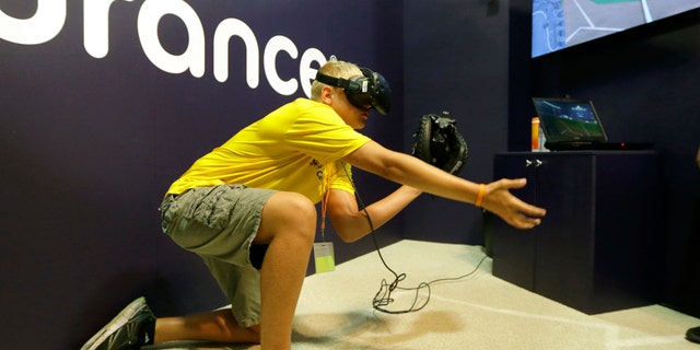 In this Friday, July 7, 2017, photo, Dennis Milman reaches to catch a virtual ball at the All-Star FanFest in Miami Beach, Fla. Virtual Reality baseball is a hit at the All-Star FanFest in Miami. Fans get to feel what it's like to be the San Francisco Giants' Buster Posey catching without the pain of snatching major league pitches at 86-to-93 mph. (AP Photo/Alan Diaz)