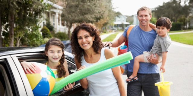 Family with two children (3 and 9 years) packing car for trip to the beach. Focus on mother and daughter.