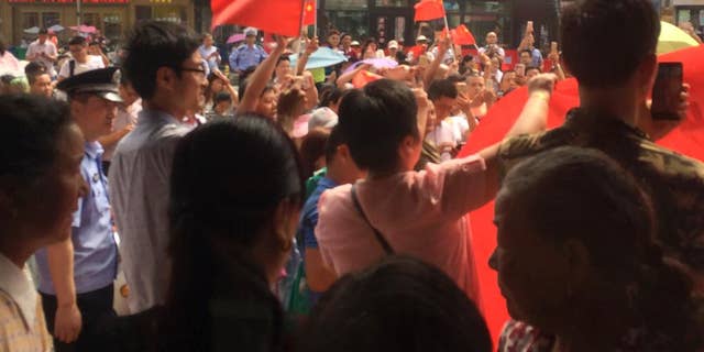 In this photo taken on Tuesday, July 19, 2016 and released by Guo Lu, policemen stand watch Chinese people carrying national flags hold a protest outside a KFC restaurant outlet in Baoying county in east China's Jiangsu province. In an apparent attempt to head off large-scale street demonstrations, Chinese state newspapers have criticized scattered protests against KFC restaurants and other U.S. targets sparked by an international tribunal's ruling that denied Beijing's claim to virtually the entire South China Sea. (Guo Lu via AP)