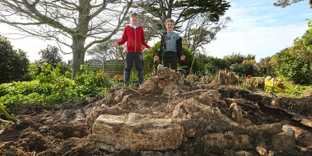 Brothers, Joe, 9 and Jake Ward, 6 with the buried Daimler which they discovered in their garden at a property in Rue du Felconte on Guernsey. See SWNS story SWCAR: These pictures show a rockery in a family's garden which turned out to be a buried 70-year-old CAR. Tracy and Chris Ward bought their home last November, but have only just set about tackling the garden. In the centre of their small plot there was an ornate rockery - or so they thought. When they started digging out the rockery they started to uncover bits of metal, and before long they had unearthed the remains of a 70-year-old Daimler Consort.