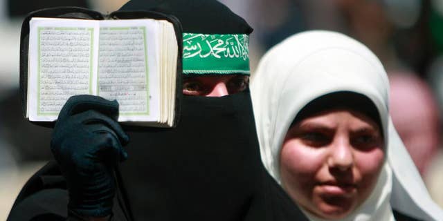 A Palestinian supporter of Hamas holds the Quran as others shout slogans against the Israeli military action in Gaza, during a demonstration in the West Bank town of Tulkarem town on Friday, Aug. 1, 2014. A Palestinian man was shot and killed during clashes with Israeli troops, following the demonstration in Tulkarem, Palestinian security sources said. (AP Photo/Mohammed Ballas)