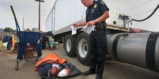 FILE - In this July 6, 2016, file photo, Ronald Mays, who rolles over to look at the flyer with pictures of a suspect in recent assaults on the homeless, as San Diego Homeless Outreach Team officer Brian Lucchesi canvasses several areas in the Midway and Sports Arena Blvd. area stopping to talk with people in San Diego. (Peggy Peattie/U-T San Diego via AP, File)