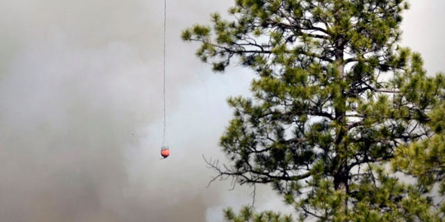 A Chinook Helicopter with a bucket heads towards the structures in the community of Ruby Hole, New Mexico. Thursday June 15, 2017. (Jim Thompson/The Albuquerque Journal via AP)