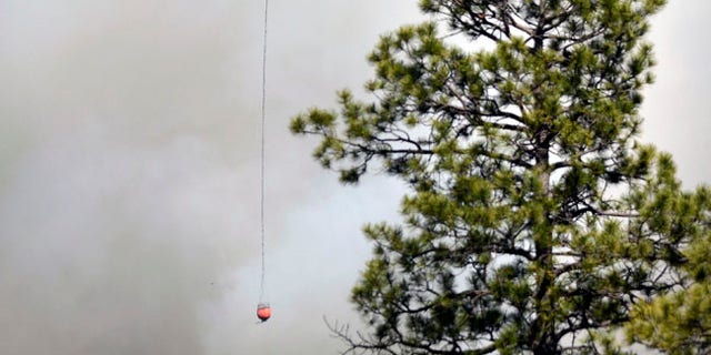 A Chinook Helicopter with a bucket heads towards the structures in the community of Ruby Hole, New Mexico. Thursday June 15, 2017. (Jim Thompson/The Albuquerque Journal via AP)