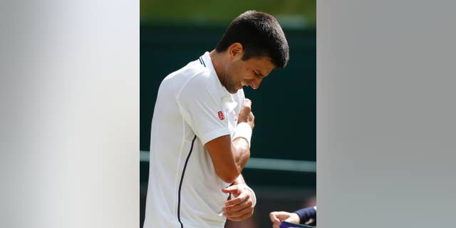 Novak Djokovic of Serbia grimaces in pain and holds his shoulder during men's singles match against Gilles Simon of France at the All England Lawn Tennis Championships in Wimbledon, London, Friday, June 27, 2014. (AP Photo/Sang Tan)