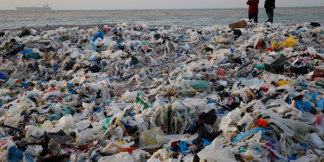 In this Monday, Jan. 22, 2018, photo, a man takes photos of piles of garbage washed on shore after an extended storm battered the Mediterranean country at the Zouq Mosbeh costal town, north of Beirut, Lebanon. Environmentalists say a winter storm has pushed a wave of trash onto the Lebanese shore outside Beirut, stirring outrage over a waste management crisis that has choked the country since 2015. (AP Photo/Hussein Malla)
