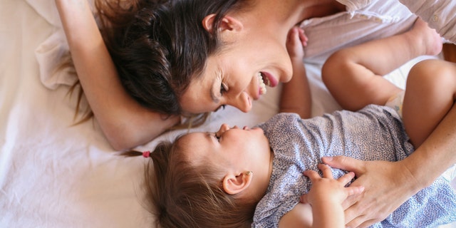 Young mother playing with her baby girl playing in bed. Space for copy.