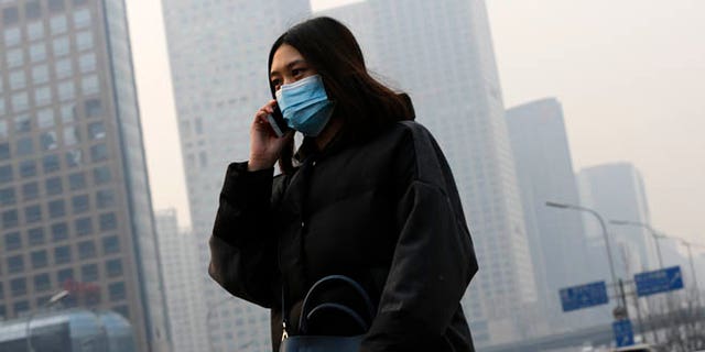 Dec. 7, 2015: A woman wearing a mask to protect herself from pollutants walks past office buildings shrouded with pollution haze in Beijing. Smog shrouded the capital city Monday after authorities in Beijing issued an orange alert on Saturday.