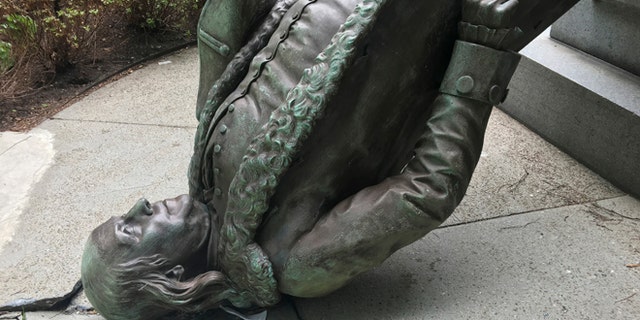 In this photo released by the City of Boston Mayor's office, a statue of Benjamin Franklin lies on the concrete outside where it landed when knocked off its pedestal outside Old City Hall