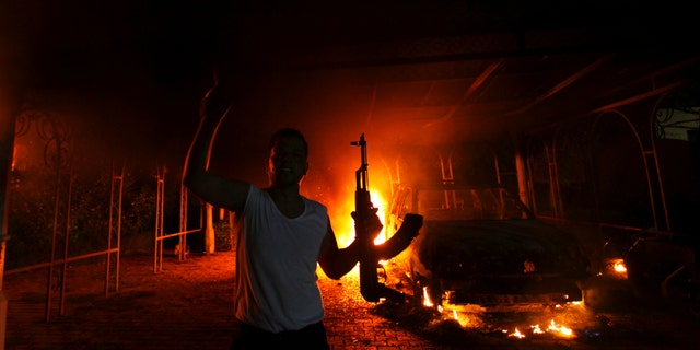 A protester reacts as the U.S. Consulate in Benghazi is seen in flames during a protest by an armed group said to have been protesting a film being produced in the United States September 11, 2012.