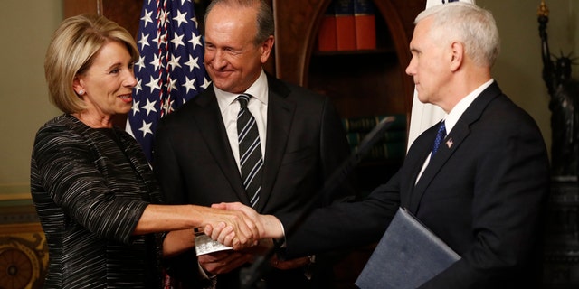 Vice President Mike Pence shakes hands after swearing in Education Secretary Betsy DeVos in the Eisenhower Executive Office Building in the White House complex in Washington, Tuesday, Feb. 7, 2016, as DeVos' husband Dick DeVos watches.