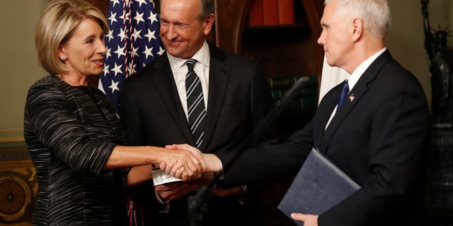 Vice President Mike Pence shakes hands after swearing in Education Secretary Betsy DeVos in the Eisenhower Executive Office Building in the White House complex in Washington, Tuesday, Feb. 7, 2016, as DeVos' husband Dick DeVos watches.