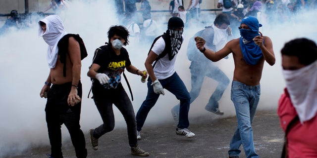Feb. 22, 2014: A group of masked men run for cover after riot police launched tear gas in Caracas, Venezuela.