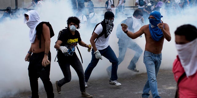 A group of masked men run for cover after riot police launched tear gas in Caracas, Venezuela, Saturday, Feb. 22, 2014. After an opposition rally broke up in the late afternoon, in a pattern that has been seen in past demonstrations about 1,000 stragglers erected barricades of trash and other debris and threw rocks and bottles at police and National Guardsmen. The troops responded with volleys of tear gas to prevent the students from reaching a highway and blocking traffic. (AP Photo/Rodrigo Abd