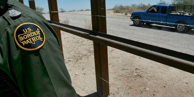 **FILE ** A U.S. Customs and Border Patrol agent is shown by the International border as a truck passes on the Mexican side of the border, in a May 24, 2006 file photo, in Arizona. Sixty three miles of vehicle barriers are in place on the Arizona border to thwart smugglers trying to bring illegal immigrants or drugs into the country in vans, SUVs and trucks. Authorities look to have a total of 200 miles of barriers across the Southwest, mostly in Arizona and New Mexico, by the end of 2008. (AP Photo/Matt York, File)