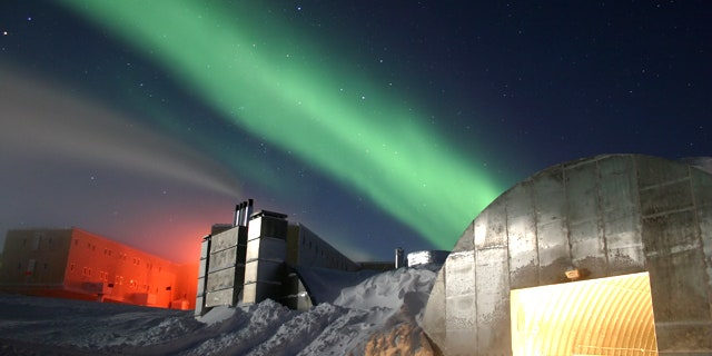 Amundsen-Scott South Pole Station during the long Antarctic night, with a new station at far left, power plant in the center and the Aurora Australis dancing through the sky.