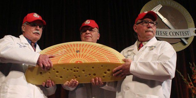 March 19, 2014: Three judges for the 2014 World Championship Cheese Contest hold the champion, a Swiss Emmentaler.